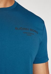 Kék pamut póló rövid ujjú, kerek nyakkivágással, fekete nyomtatott szöveggel: "BJÖRN BORG" és "STOCKHOLM 1956."