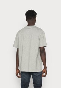 Gray cotton t-shirt with short sleeves, crew neckline, relaxed fit, and smooth texture, viewed from the back, paired with dark jeans.
