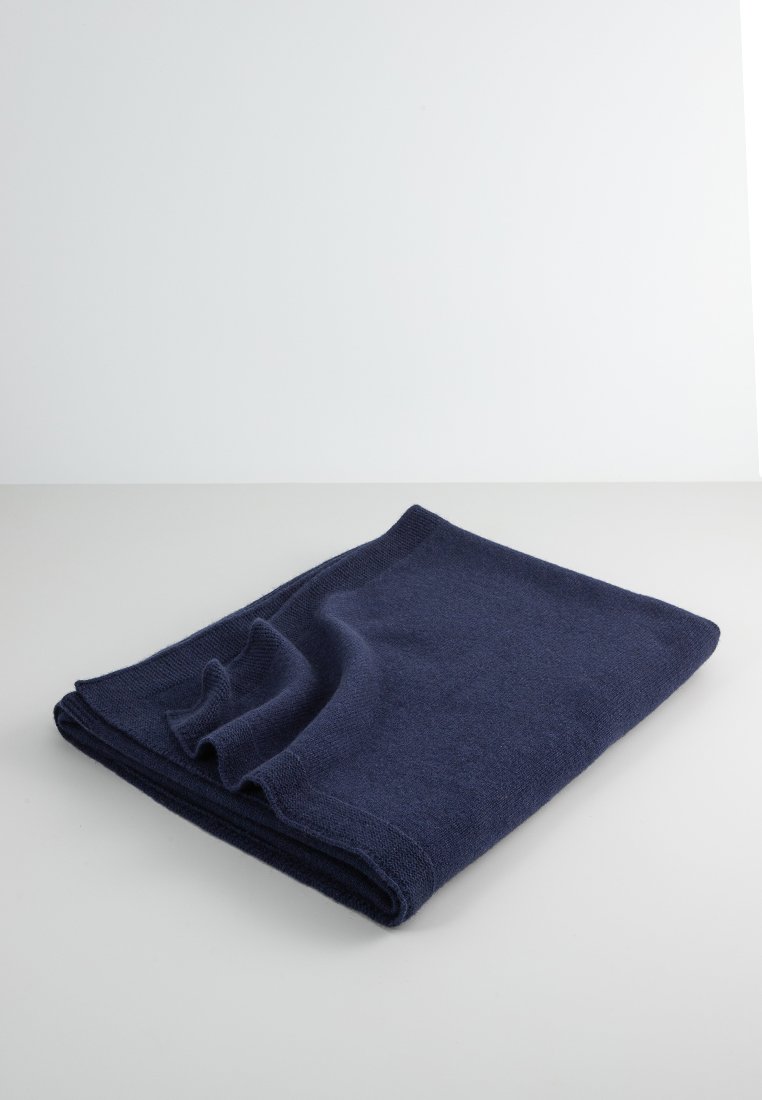 Manta de punto azul marino, forma rectangular, textura suave, con sutiles pliegues, presentada sobre una superficie gris claro.