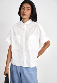 White short-sleeve shirt with a collared neckline, two front pockets, and a slightly loose fit; fabric appears smooth and crisp.