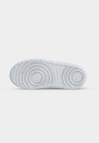Hvid sneakersål med cirkulære slidmønstre og små Nike-logoer på en ensfarvet lys baggrund.