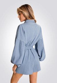 Salopette in denim blu chiaro con vita aderente, maniche lunghe a palloncino e collo a camicia, caratterizzata da uno stile shorts rilassato.
