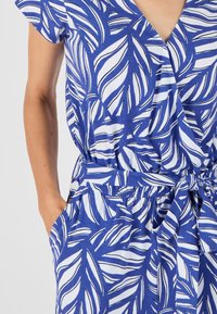 Robe à motifs bleus et blancs avec des motifs de feuilles, à manches courtes, décolleté en V, taille élastique, poches latérales et ceinture à nouer.