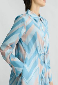 Abito a maniche lunghe in blu chiaro e rosa con motivo a zigzag, realizzato in tessuto morbido. Presenta un colletto e chiusura con bottoni.