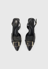 Juodos odinės slingback kulniukai su smailiu priekiniu dalimi, puikuojasi auksiniu sagtimi ant dirželių. Lygi tekstūra ir liekna forma.