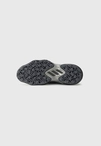 Semelle en caoutchouc noir avec un motif de semelle complexe et trois bandes noires sur un fond argenté au niveau de la voûte plantaire de la chaussure.