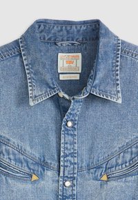 Lichtblauwe denim shirt met een puntige kraag, drukknoopsluiting, borstzakken en gouden accenten. Het heeft een gestructureerde stof met zichtbare stiksels.