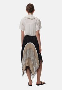 Zwarte geplooide rok met een beige golfpatroon en kantdetail, gecombineerd met een witte top met korte mouwen. De zoom is asymmetrisch, wat een vloeiende silhouet creëert.