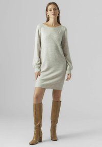Abito maglione grigio chiaro con scollo a barca e maniche lunghe a sbuffo, abbinato a stivali in pelle beige alti fino al ginocchio.
