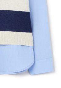 Camicia a collo blu indossata sotto un maglione a righe crema e blu navy. Texture in maglia con dettagli a costine sull'orlo e sui polsini; finitura in tessuto liscia.