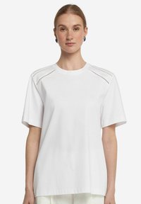 Hvid bomulds T-shirt med korte ærmer, med perforerede detaljer på skuldrene og en rund halsudskæring. Glat tekstur og afslappet pasform.