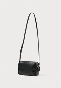Černá prošívaná crossbody taška s obdélníkovým tvarem, hladkým koženým materiálem, zipovým uzávěrem a nastavitelným popruhem.