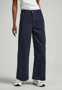 Jūras spēku platleņķa džinsi, izgatavoti no džinsa auduma, ar priekšējo pogu aizdari, piecu kabatu dizainu un brīvu piegriezumu ar nelielu izbalējumu.