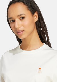 Weißes Baumwoll-T-Shirt mit rundem Ausschnitt und kleinem gesticktem Tierdesign auf der Brust. Glatte Textur und lässige Passform.