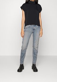 Top nero a maniche corte con collo alto, abbinato a jeans in denim azzurro chiaro e stivaletti neri con zeppa. Tessuto morbido e vestibilità comoda.