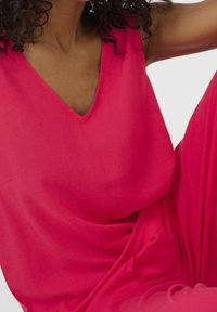 Haut rose sans manches avec un décolleté en V. Confectionné dans un tissu lisse, il présente une coupe décontractée avec des plis subtils.