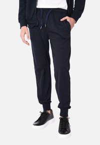 Pantaloni felpa blu navy realizzati in un tessuto morbido, dotati di una vita elastica con cordino e tasche laterali. Indossati con sneakers nere.