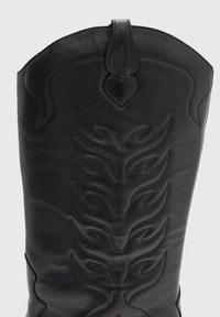 Svart läder cowboystövel med sydd flamamönster, spetsig tå och en dekorativ dragflik med präglad logga längst upp.