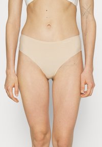 Beige bikini briefs made of smooth, stretchy material. Mid-rise design with a seamless finish and Calvin Klein logo on the waistband.