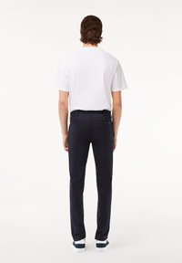 Conjunto masculino que incluye una camiseta blanca básica, pantalones azul marino y zapatillas blancas con detalles en azul marino. Los pantalones tienen una textura lisa y un corte ajustado.