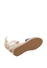 Ekspadril sandaalid jute-kootud tallaga, beežide rihmadega ja sinise varvaste paneeliga. Omab tekstureeritud kummitalda haarde saavutamiseks.