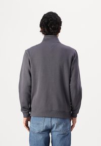 Pullover grigio con colletto alto, dotato di polsini e orlo a coste. Indossato con jeans in denim azzurri, che mostrano un design semplice.