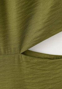 Tkanina oliwkowa o teksturowanej powierzchni, z detalem wycięcia i kieszenią. Projekt zawiera proste linie i gładkie wykończenie.