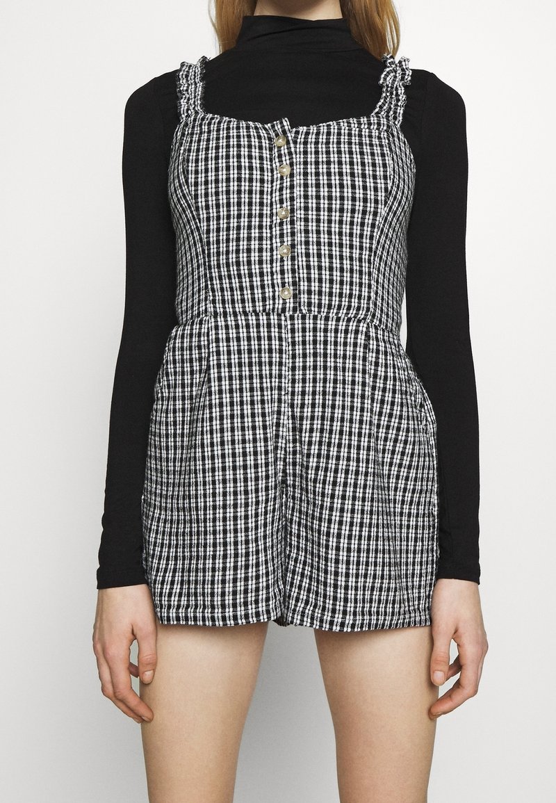 Svartvit rutigt klänning med en åtsittande överdel, knapplist fram och volangaxlar. Kombinerad med en svart långärmad tröja under.