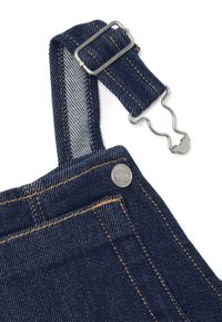 Denim tuinbroek band met metalen verstelbare gesp en golvende sluiting, gedetailleerd met oranje stiksel en een gemerkte metalen knop.