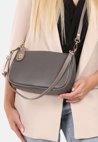 Grijze leren handtas met een textuur, voorzien van een afneembare schouderband en gouden accenten. Het heeft een rechthoekige vorm met afgeronde hoeken.