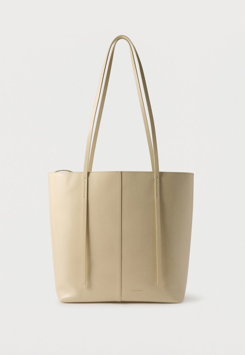 Τσάντα tote από μπεζ δέρμα με δύο μακριές ιμάντες ώμου και ένα απλό κάθετο ρέλι στη μέση.