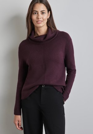 Pull à col bénitier bourgogne en tissu doux avec des manches longues, présentant un détail de couture sur le devant et une coupe décontractée, associé à un pantalon noir.