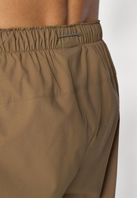 Shorts à taille élastique marron avec une texture lisse, présentant un tissu froncé et un subtil détail de couture.