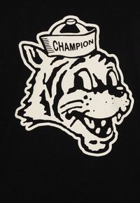 Mustapea T-särk, millel on suur, valge graafika naeratava joonistatud tiigri peast, kes kannab "Champion" mütsi. Julged jooned toovad disaini esile.