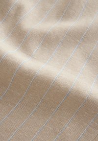 Hellbeige Stoff mit strukturiertem Gewebe, der dünne blaue Streifen vertikal aufweist. Weiche Textur und leicht zerknittertes Erscheinungsbild.