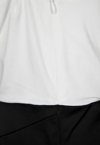 Vit topp med samlad textur som övergår till en enfärgad svart nederdel. Har en dold dragkedja bak och minimal sömsdetalj.
