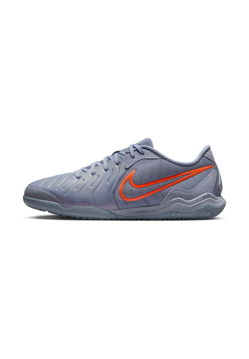 Világos lila sportcipő, textúrált felülettel, a kiváló narancssárga Nike logóval az oldalon és szürke gumitalppal.