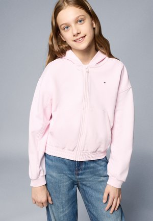 Lichtroze hoodie met rits, voorzien van een voorzak en elastische tailleband, met ribkraag cuffs. Gepaard met blauwe denim jeans.
