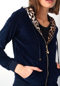 Námořnická modrá mikina na zip vyrobená z měkkého sametu, s leopardím potiskem podšívky kapuce a bočními kapsami se zlatým zipem.