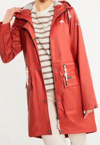 Red waterproof jacket with a gray hood, silver zipper, and front pockets. Features drawstrings with beads and an umbrella logo on the chest.