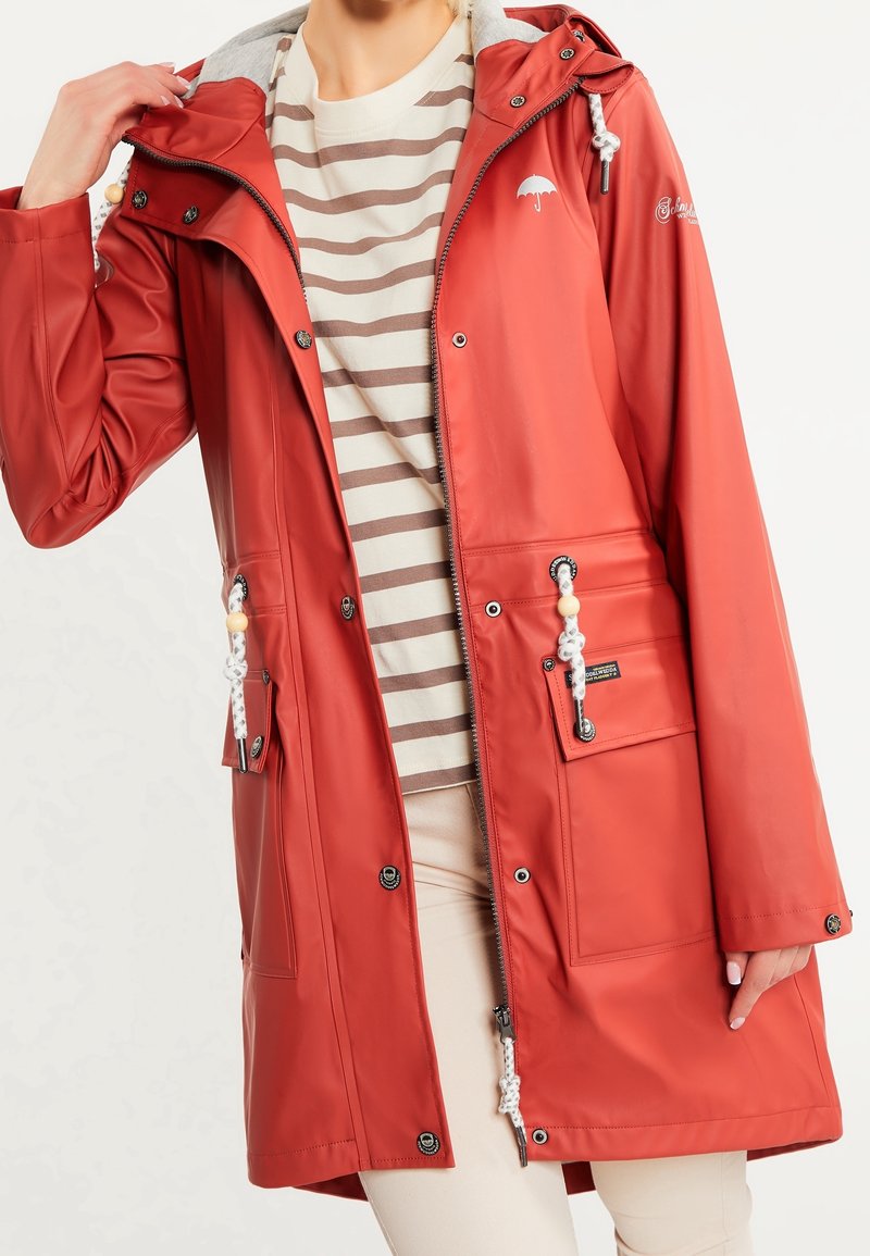 Red waterproof jacket with a gray hood, silver zipper, and front pockets. Features drawstrings with beads and an umbrella logo on the chest.