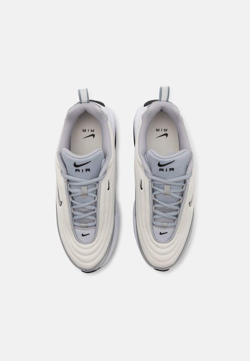 Zapatillas Nike Air con parte superior en color crema, detalles en gris, superposiciones texturizadas y suela negra. Cuentan con cordones y una lengüeta en el talón para facilitar su puesta.