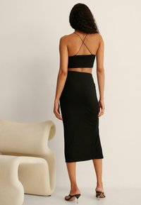 Mustat ribattut bodycon-mekot, joissa on lyhyt yläosa ja spagettiolkaimet. Ominaisuuksina istuva siluetti ja polvipituinen hame. Suuri tekstuuri.