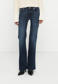 Tmavomodré zvonové rifle z denimu s klasickým päťvreckovým dizajnom a jemným prešitím. Kombinované s krémovým svetrom.