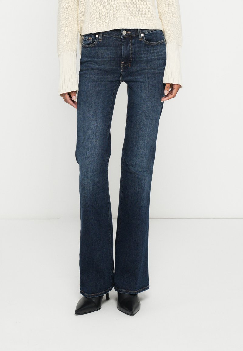 Tmavomodré zvonové rifle z denimu s klasickým päťvreckovým dizajnom a jemným prešitím. Kombinované s krémovým svetrom.