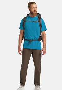 Blaues kurzärmeliges Hemd und braune Hose, getragen von einer Person mit einem schwarzen Rucksack, der verstellbare Gurte und mehrere Taschen aufweist.