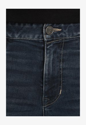 Donkerblauwe denim jeans met een metalen knoopsluiting, contrasterende stiksels en een klassieke vijf-pocket ontwerp. De textuur lijkt iets versleten.