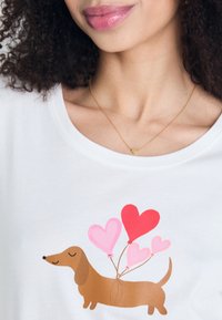 Fehér póló, amelyen egy barna tacskó grafika látható négy színes, rózsaszín és piros szív alakú lufival.