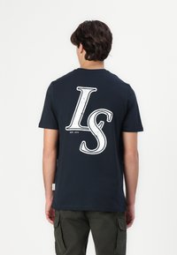 Tamsiai mėlynas medvilninis marškinėliai su dideliu baltu "LS" grafiku nugaros pusėje. Trumpi rankovės ir apvalus kaklas. Laisvas siluetas.
