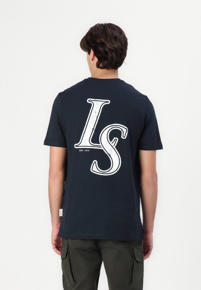 Jūras zilas kokvilnas T-krekls ar lielu baltu "LS" grafiku uz muguras. Īsas piedurknes un apaļa apkakles forma. Brīvs piegriezums.